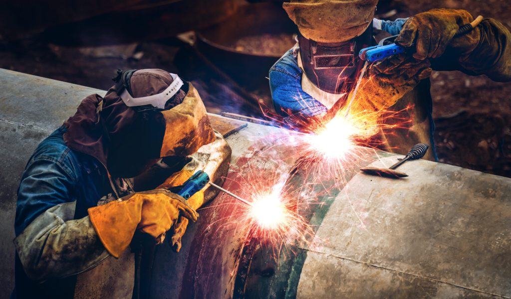 Workers with protective masks welding bore pile metal casing at a construction site